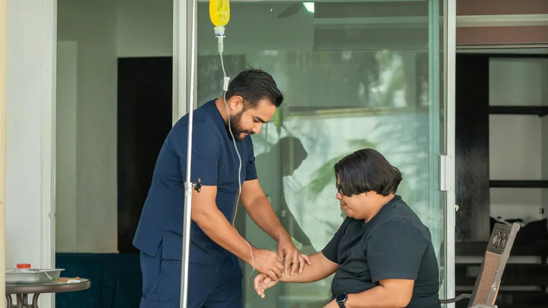 Clinician attending to a seated patient on a home veranda, with an IV stand beside them.