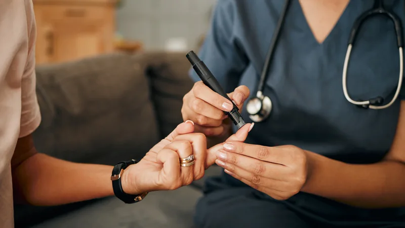 Healthcare professional checking a patient’s blood glucose with a finger-prick test.